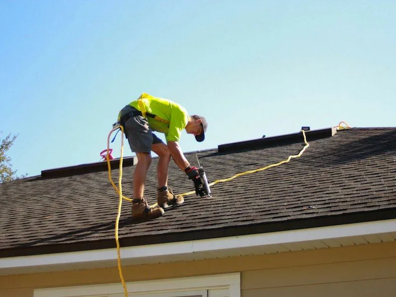 A roofer in a harness working on an asphalt shingle roof
