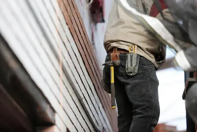A roofer carrying hand tools across a shingle roof